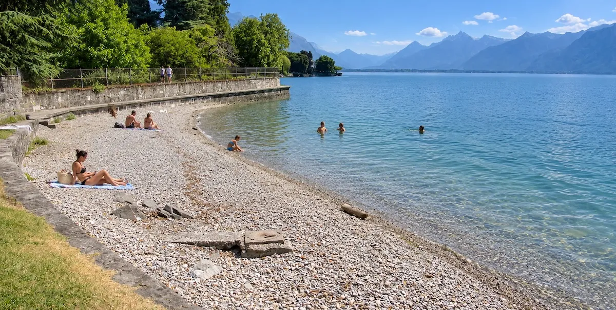 Plage de galets de la Maladaire à La Tour-de-Peilz, au pied d'un mur de pierre, baigneurs dans le Léman